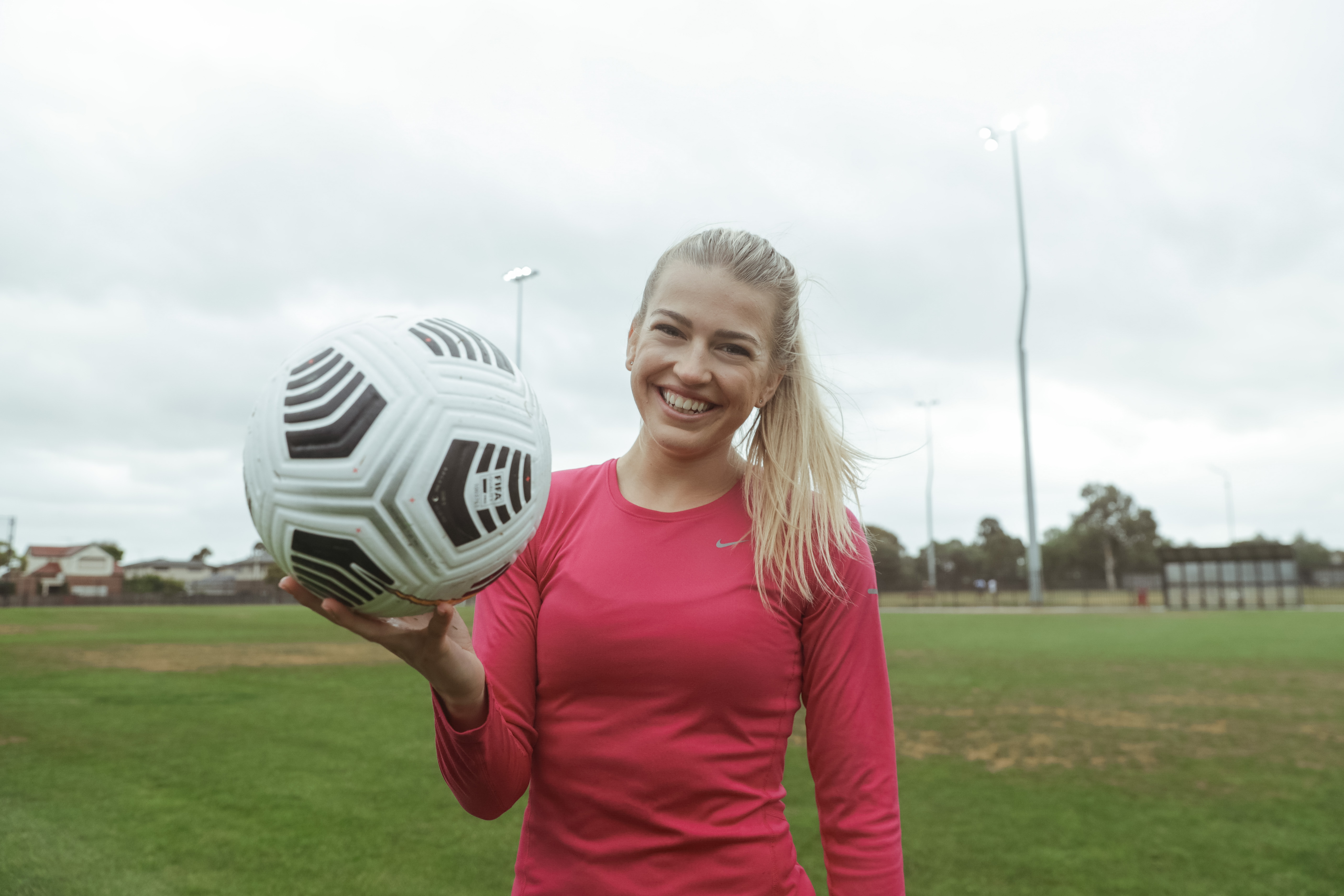 Charli Grant smiling at the camera whilst holding up a football
