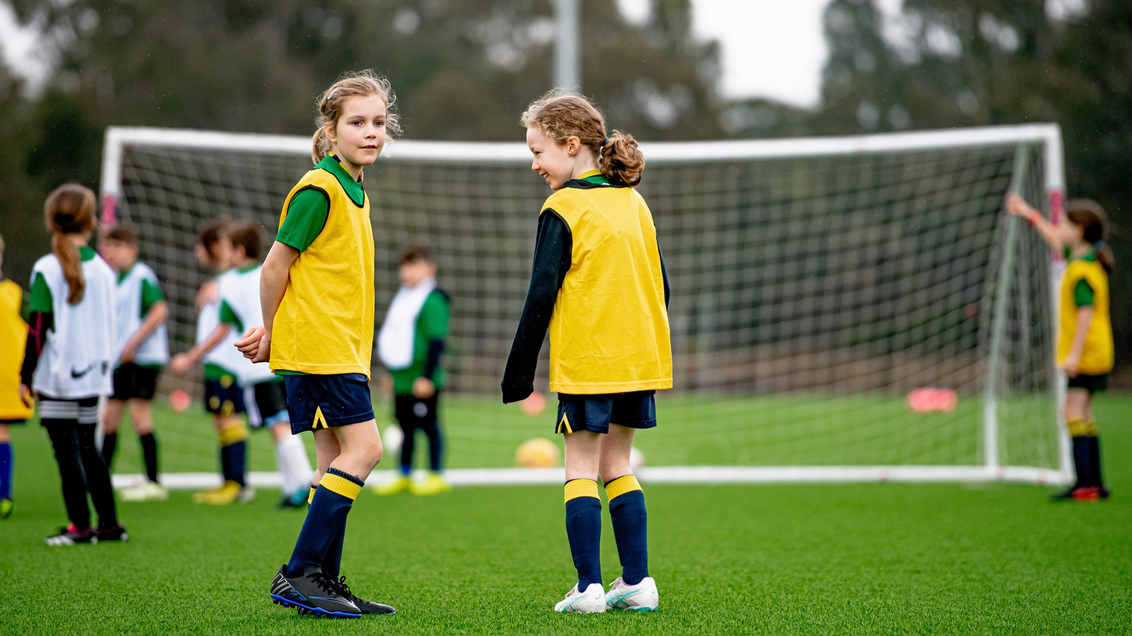 Image focuses on two young female football players in green and yellow.