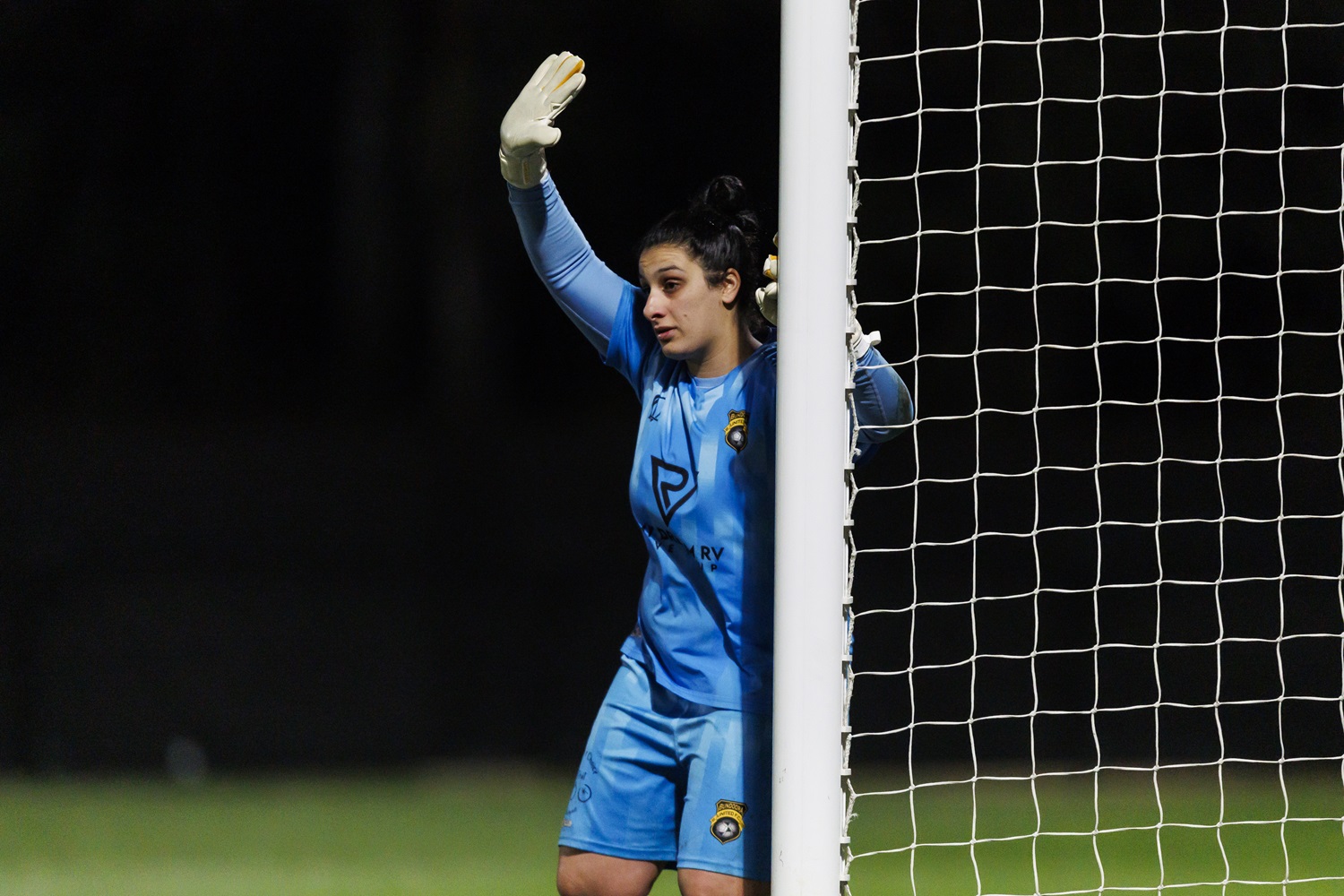 Bundoora United next to the post with right hand up at night.