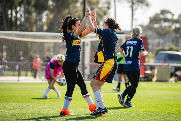 Female playing football and celebrating with arms up, high fiving.