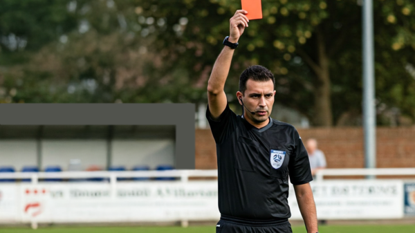 Referee holding up red card on community soccer pitch